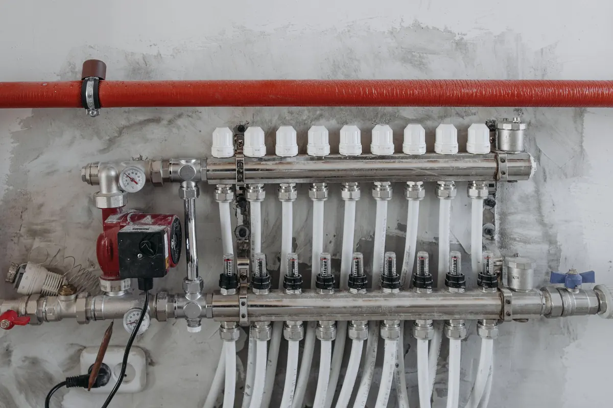 Verdeler van vloerverwarming met witte leidingen aan een muur